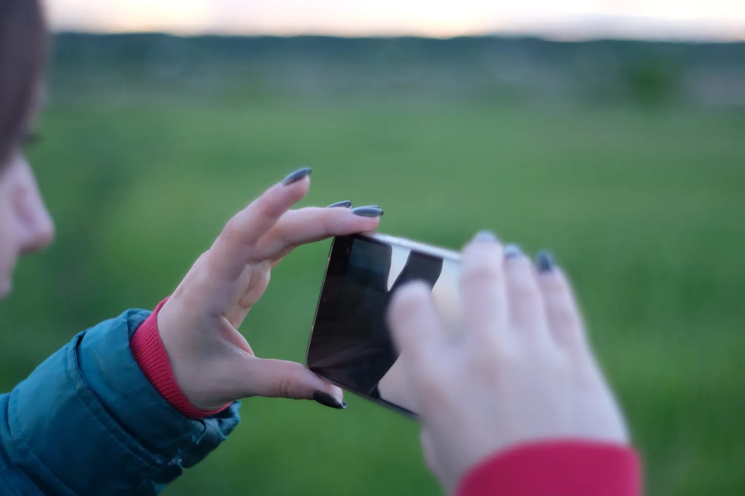 Close-up of a woman photographing a green meadow